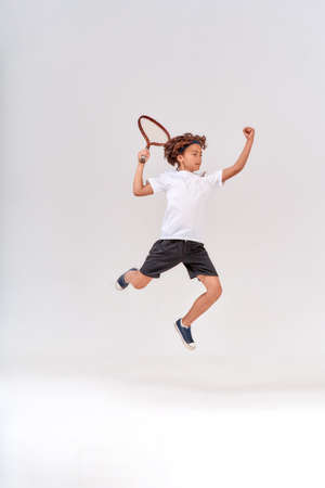 Little winner. Full-length shot of a teenage boy jumping with a tennis racket isolated over grey background, studio shot.の写真素材