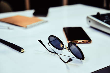 Close up of stylish sunglasses, pen and smartphone on a table in radio station studioの写真素材