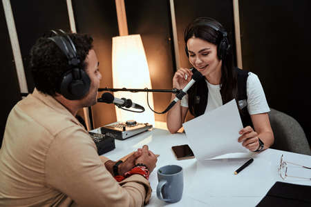 Portait of happy female radio host smiling, talking to male guest, presenter while moderating a live show in studioの写真素材
