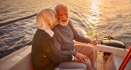 Romantic evening on the boat. Portrait of happy senior couple holding hands, hugging and kissing