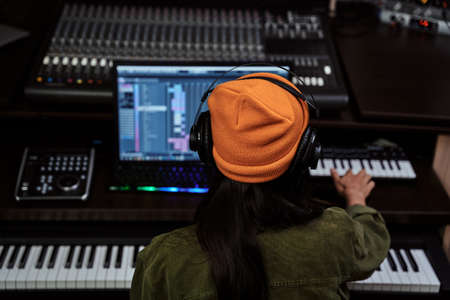 Portrait of beautiful young brunette, female artist playing keyboard synthesizer, sitting in recording studioの写真素材