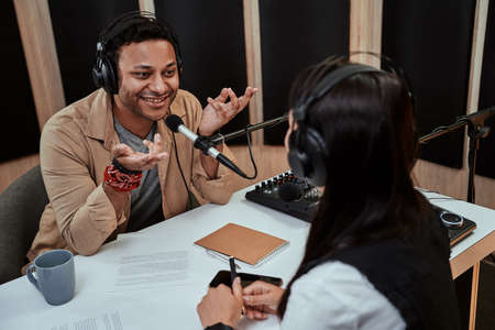 Portait of happy male radio host smiling, talking to female guest while moderating a live show in studioの写真素材