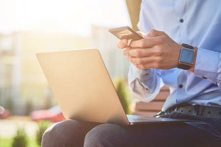 Online business. Cropped shot of a businessman using smartphone and laptop while sitting on the...
