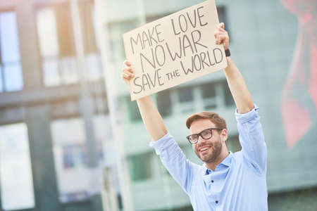 Save the world. Happy young male activist holding banner or poster over the head while protesting against war, standing on the roadの写真素材