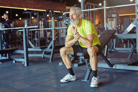 Taking a break. Exhausted mature man in sportswear resting after hard workout at gymの写真素材