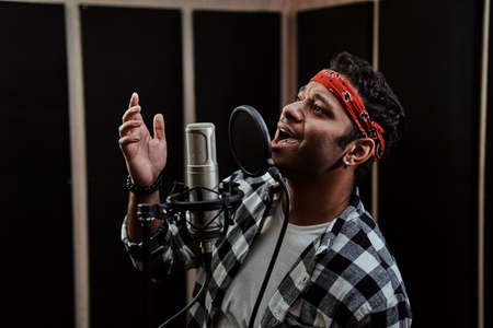 Portrait of young man, hip hop artist enjoying the process of singing into a condenser microphone while recording a song in a professional studioの写真素材
