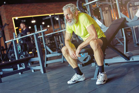 Exhausted mature man in sportswear resting after hard workout at gymの写真素材