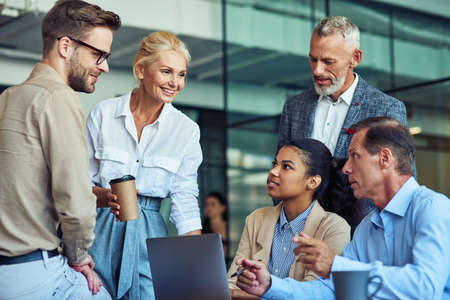 Having a meeting. Group of multiracial business people in classic wear working together on a new project while sitting together in the office, using laptopの写真素材