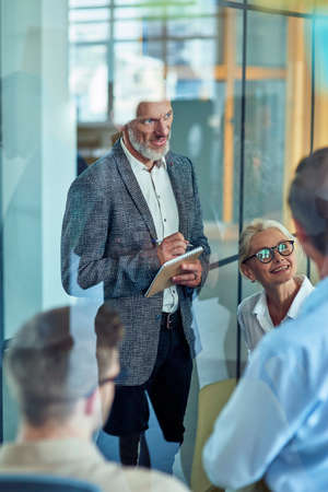 Office life. Vertical shot of a handsome mature businessman making some notes while having a meeting with coworkers in the modern officeの写真素材