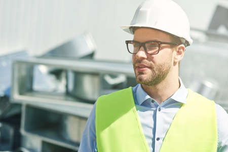 Portrait of young civil engineer wearing helmet looking away while standing at construction siteの写真素材