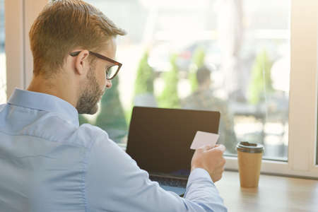 Rear view of a young businessman looking at blank business card while working remotely in cafeの写真素材