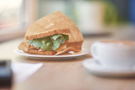 Fresh breakfast. Cup of coffee and sandwich on wooden table in cafe, selective focusの写真素材