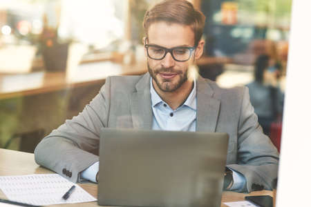 Front view of a young busy caucasian businessman or male freelancer using laptop while working remotely in cafeの写真素材