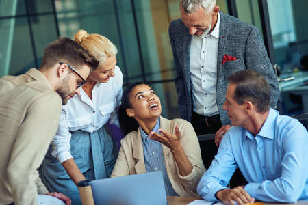 Group of multiracial business people in classic wear looking at laptop screen and discussing new project while working together in the modern officeの写真素材