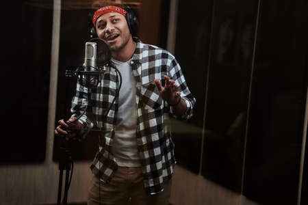 Portrait of young man, male artist looking focused, singing into a condenser microphone while recording a song in a professional studioの写真素材