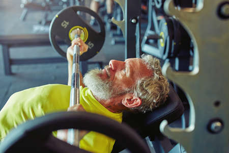 Pushing the limits of human body. Side view of a mature caucasian man lifting weighted bar or barbell at gymの写真素材
