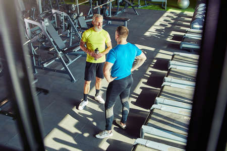 Full length shot of a middle aged man in sportswear talking with fitness instructor or personal trainer while working out at gym or sport clubの写真素材
