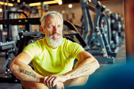 Portrait of a middle aged man discussing workout plan with fitness instructor while sitting together on the floor at gymの写真素材