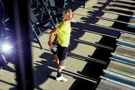 Full length shot of a mature athletic man in sportswear doing stretching exercises, warming up before workout in a gymの写真素材