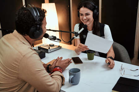 Portait of happy female radio host smiling, talking to male guest, presenter while moderating a live show in studioの写真素材