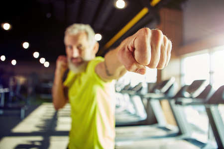 Strength training. Focused mature man in sportswear boxing, while working out at gym, focus on male handの写真素材