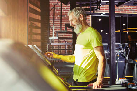 Cardio workout. Side view of a happy middle aged athletic man in sportswear adjusting speed on a...