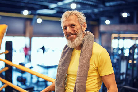 Resting after boxing training. Portrait of a positive handsome mature man in sportswear looking at camera and smiling while standing on the ring at gymの写真素材