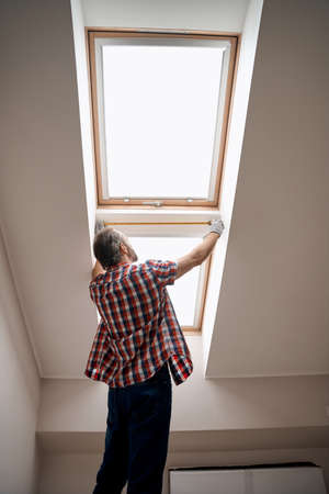 Back view of worker leaning measuring tape on windowの写真素材