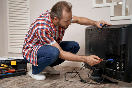 Young caucasian repairman mending tv receiver with screwdriverの写真素材