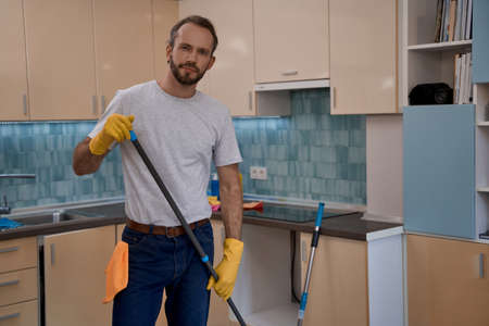 Young caucasian man in yellow rubber gloves holding mopの写真素材