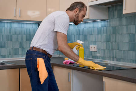 Young caucasian male worker polishing worktop with cleaning clothの写真素材
