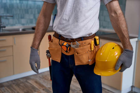 Worker with instrument belt and helmet standing in kitchen