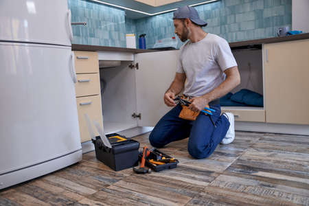 Young caucasian repairman looking into drawer under sinkの写真素材