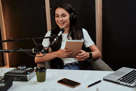 Portait of attractive young female radio host holding a script, looking emotional while speaking in microphone, moderating a live showの写真素材