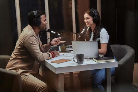 Portait of two happy radio hosts, young man and woman smiling while discussing various topics, moderating a live show in studioの写真素材