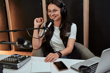 Portait of attractive young female radio host looking cheerful while speaking in microphone, moderating a live showの写真素材