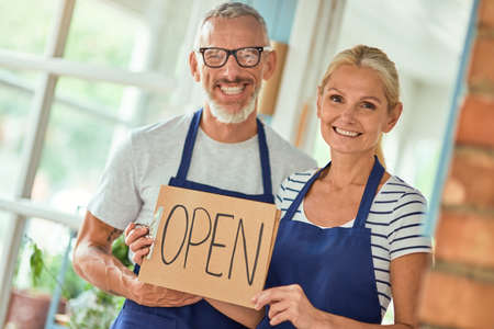 Middle aged caucasian spouses holding open shop sign