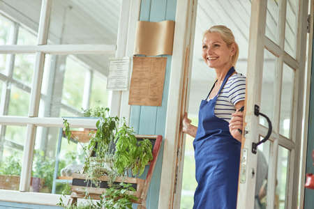 Middle aged woman holding handle on garden house doorの写真素材