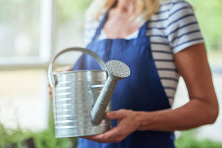 Woman holding watering can in hands standing in greenhouseの写真素材