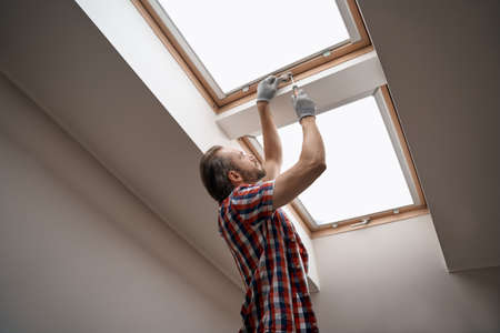Young caucasian worker screwing skylight window handleの写真素材