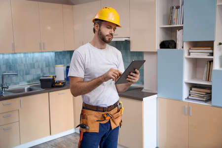 Builder in helmet working with tablet on kitchen backgroundの写真素材