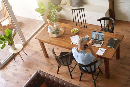 Top view of a mature caucasian businessman sitting at table in his modern apartment and working online on laptopの写真素材