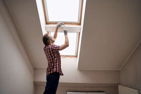 Young caucasian repairman screwing handle on skylight windowの写真素材