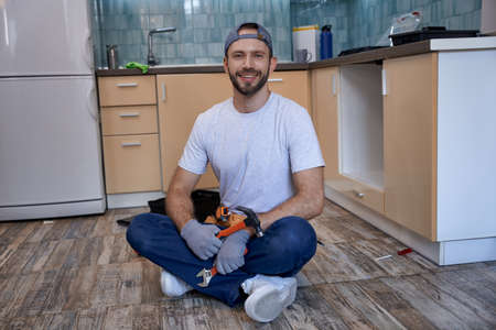 Happy young caucasian workman sitting on kitchen floorの写真素材