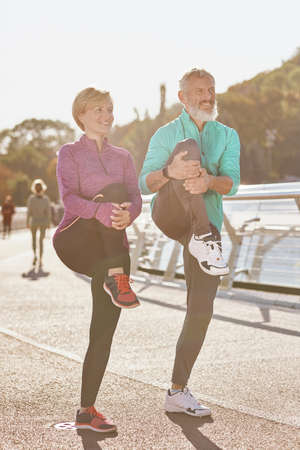 Healthy body. Full length shot of mature man and woman in sportswear smiling, stretching legs while warming up together outdoors in the morningの写真素材