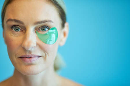 Pretty lady applying medical eye patches isolated on blue background