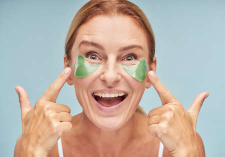 Happy mature lady moisturizing skin around her skin while using patchesの写真素材