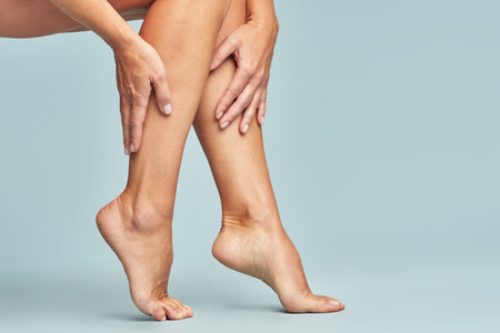 Cropped shot of a woman touching her legs with smooth, silky and soft skin after making a depilation, sitting over blue backgroundの写真素材