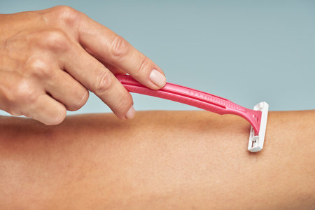 Close up of lady shaving her leg with safety razor isolated on blue backgroundの写真素材