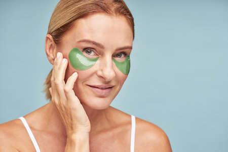 Happy Caucasian woman with hydrogel eye patches posing on blue studio wallの写真素材